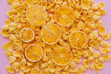 top view of dried oranges on top of crispy breakfast corn flakes isolated on pink clipart