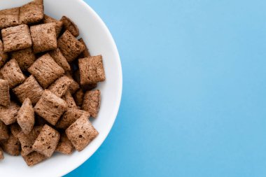 top view of chocolate cereal puffs in white bowl isolated on blue clipart