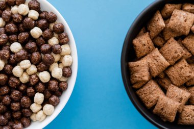top view of bowls with tasty cereal balls and puffs isolated on blue clipart