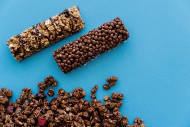 Çıtır müsli yakınlarındaki granola barlarının üst görünümü mavi üzerine izole edilmiş 