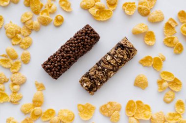 Beyaz üzerinde izole edilmiş gevrek mısır gevreğinin etrafındaki lezzetli granola barlarının üst görüntüsü 