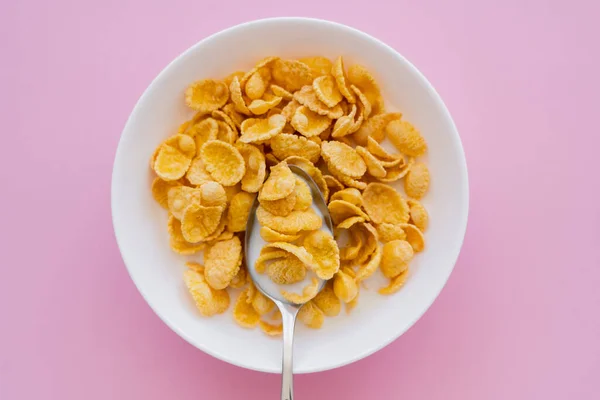 粉红背景的玉米片 牛奶和勺子碗的顶部视图 — 图库照片