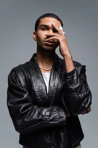 young african american man in leather jacket covering face isolated on grey