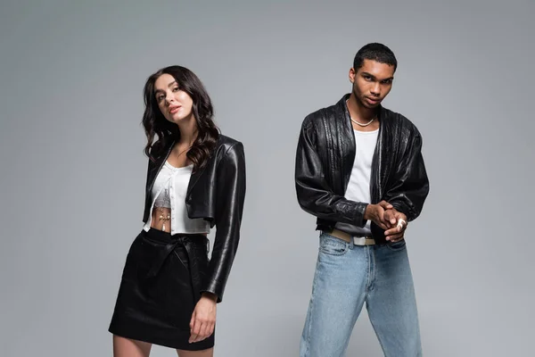 young interracial couple in black leather jackets looking at camera isolated on grey