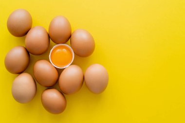 Sarı arkaplandaki yumurtaların yanındaki kabuklu yumurta sarısının üst görüntüsü 