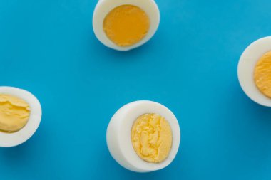 Top view of cut boiled eggs on blue surface  clipart