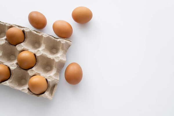 Top view of brown eggs near carton packages on white background with copy space