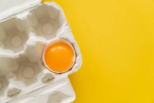 黄色の背景にカートンボックスのシェルで新鮮な卵の黄身のトップビュー — ストック写真