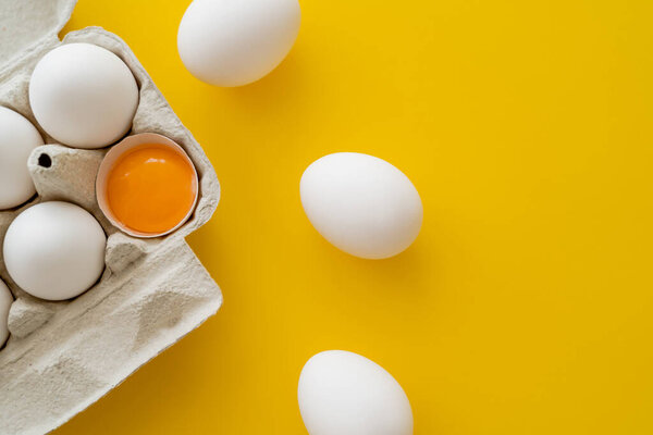 Top view of eggs near fresh yolk in shell in container on yellow background 