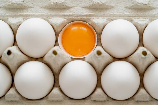 Top view of fresh yolk in shell near white eggs in cardboard tray 
