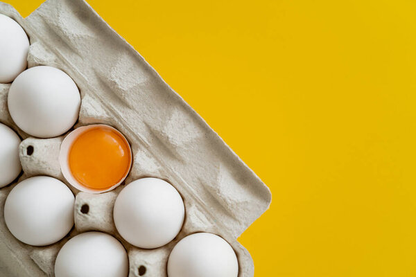 Top view of natural yolk in shell near eggs in carton box isolated on yellow 