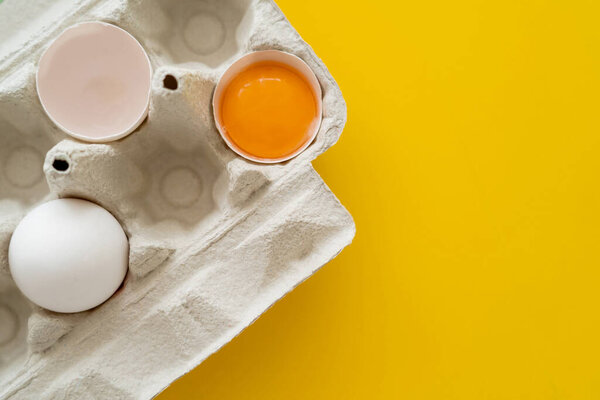 Top view of yolk near shell and egg in cardboard box on yellow background 