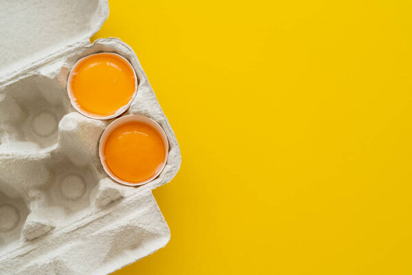 Top view of fresh yolks in shells in egg tray on yellow background 