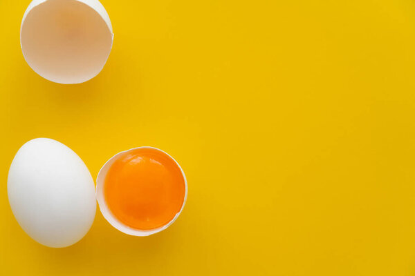 Top view of natural yolk in shell near white egg on yellow background 
