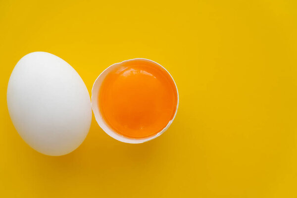 Top view of white egg near raw yolk in shell on yellow background 