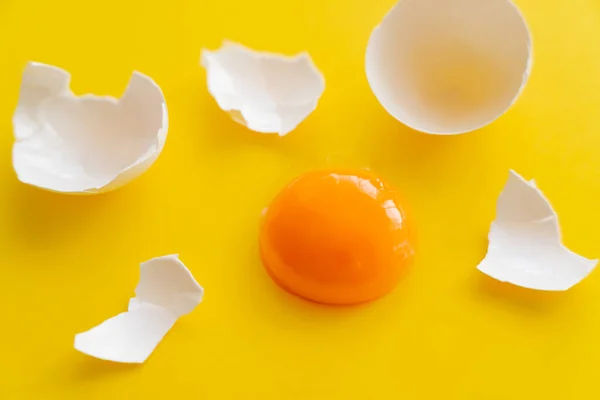 黄色の背景に割れた卵の殻の近くに生の黄身のビューを閉じます — ストック写真