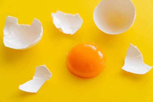 Close up view of raw yolk near cracked egg shell on yellow background 