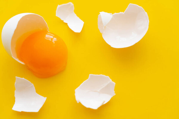 Top view of white egg shell near raw yolk on yellow background 