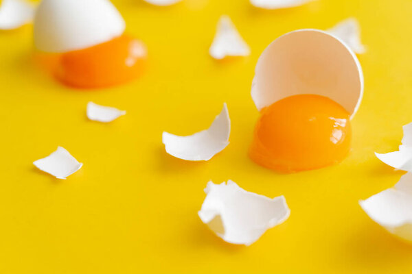 Close up view of fresh yolk and cracked egg shells on yellow surface 