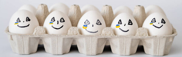 Painted eggs with facial expression and ukrainian flag in container on white background, banner 