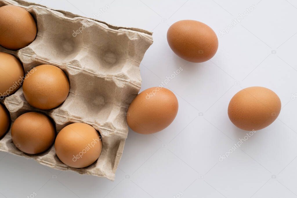 Top view of brown eggs near carton box on white background 