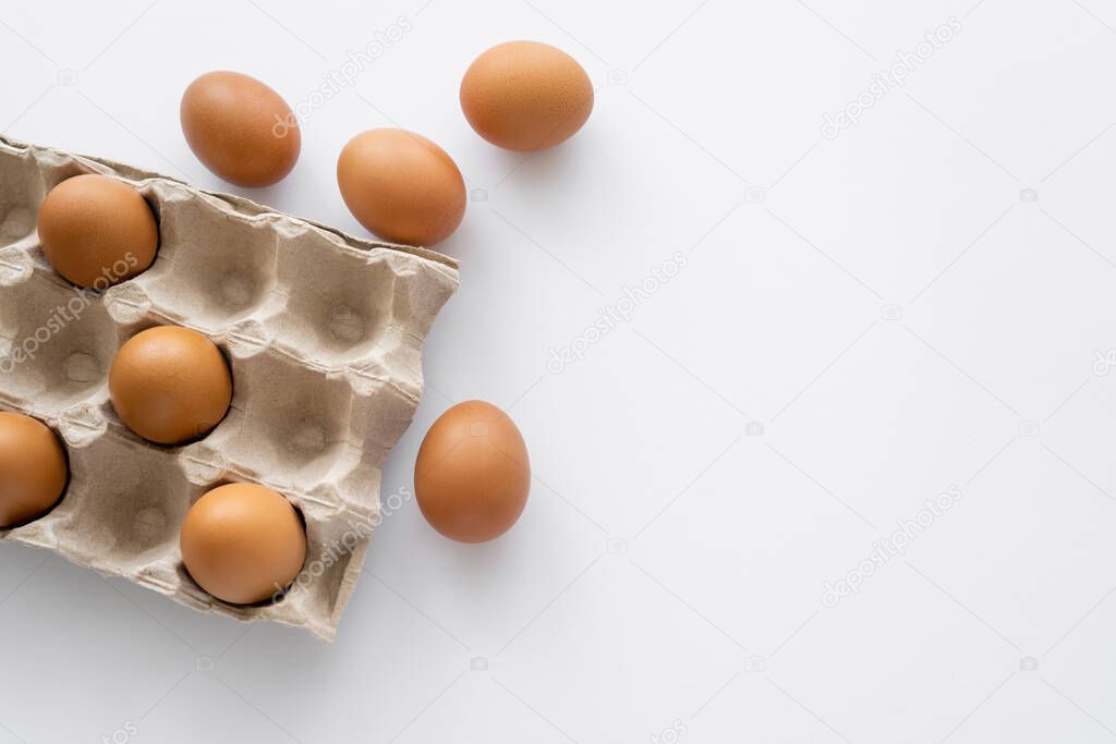 Top view of brown eggs near carton packages on white background with copy space