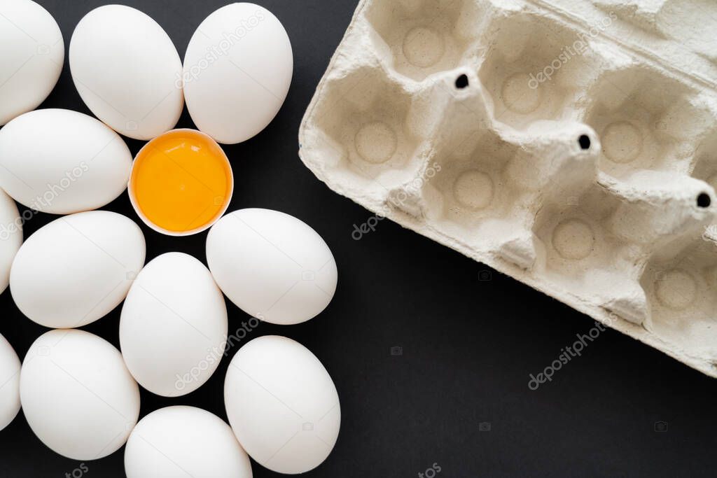 Top view of carton tray near white chicken eggs on black background 