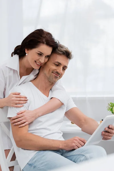 Smiling Woman Shirt Embracing Husband Using Digital Tablet Kitchen — Stock Photo, Image