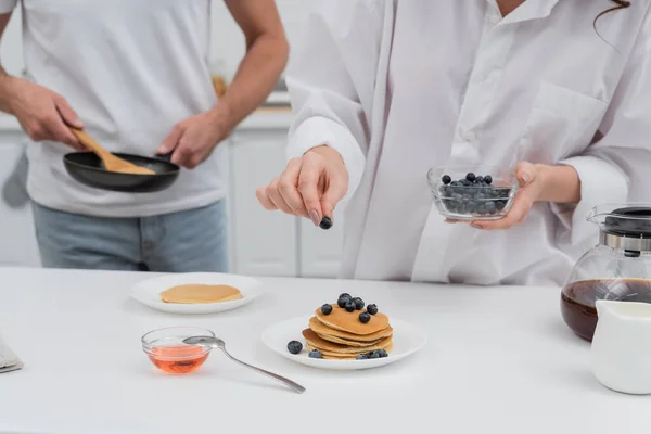 Cropped View Woman Holding Blueberries Pancakes Blurred Husband Frying Pan — Stock Photo, Image