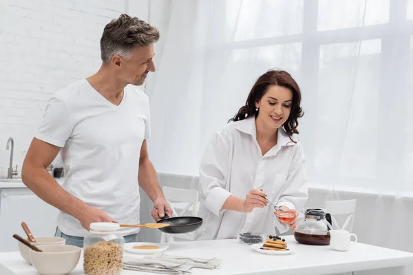 Mujer Sonriente Sosteniendo Miel Cerca Panqueques Marido Con Sartén Cocina —  Fotos de Stock