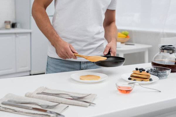 Cropped view of man holding pancake and frying pan near coffee and honey in kitchen 