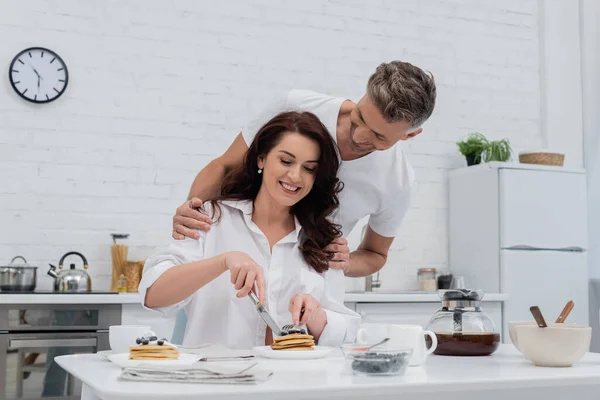 Man Hugging Smiling Wife Shirt Cutting Pancakes Kitchen — Stock Photo, Image