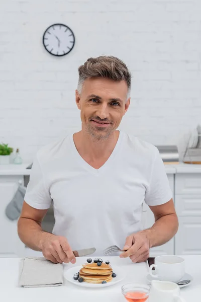 Sorrindo Homem Olhando Para Câmera Perto Panquecas Com Mirtilos Cozinha — Fotografia de Stock
