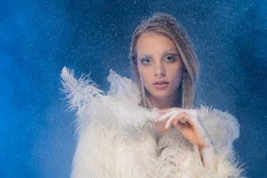 Kışın makyajlı genç bir kadın koyu mavi kar altında beyaz tüy tutuyor. 