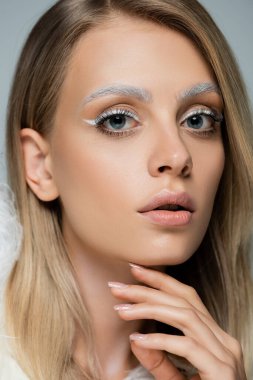Kışın makyajlı ve donmuş beyaz kaşlı genç modelin gri renkli görüntüsü.