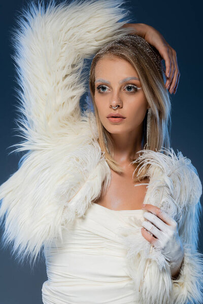 young blonde woman with piecing posing in white faux fur jacket on dark blue