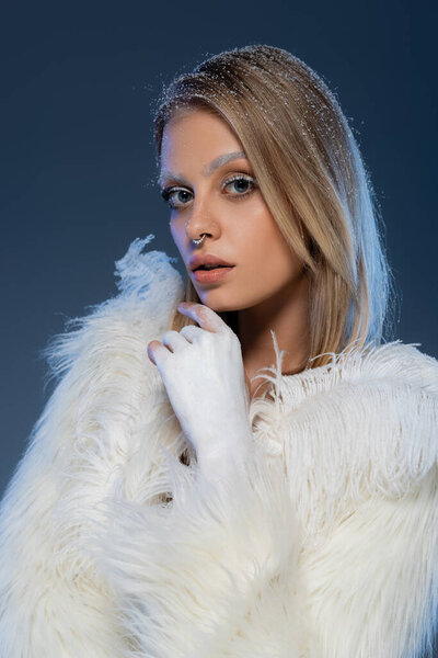 young woman with winter makeup posing in faux fur jacket with feathers on dark blue 