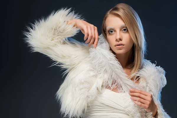blonde woman in faux fur jacket posing with white feather isolated on blue
