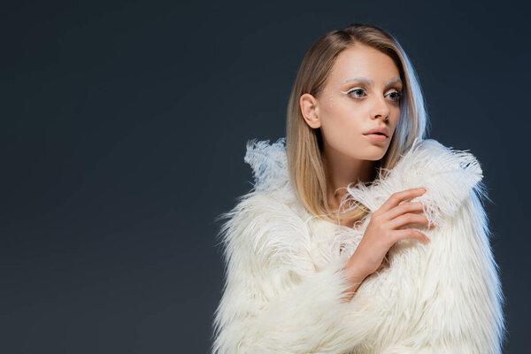 blonde young woman with white makeup posing in jacket and looking away isolated on blue