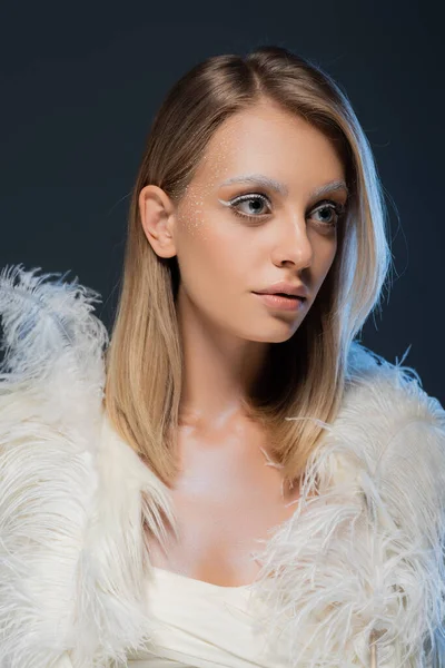 young woman in faux fur jacket with white feathers looking away isolated on blue