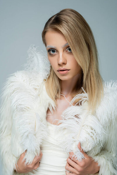 young woman in stylish faux fur jacket with feathers posing isolated on grey