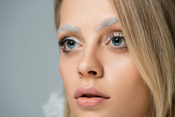 close up view of young model with winter makeup and frozen white eyebrows looking away isolated on grey