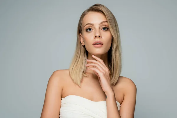 young blonde woman with blue eyes and natural makeup looking at camera isolated on grey