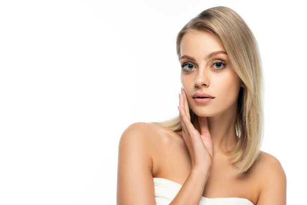portrait of blonde woman with bare shoulders and blue eyes touching face isolated on white