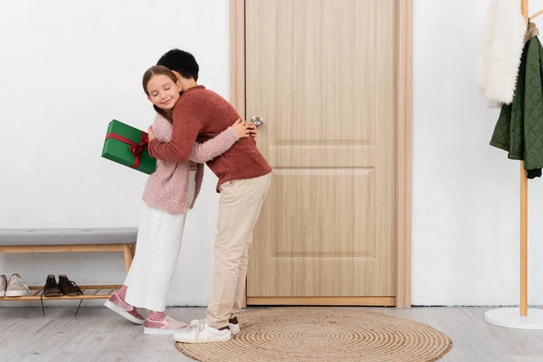 Menino Abraçando Amigo Sorridente Segurando Presente Perto Porta Casa — Fotografia de Stock