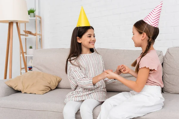 Smiling Girls Party Caps Holding Hands Birthday Party Couch Home — Stock Photo, Image