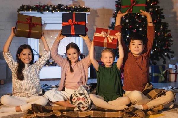 クリスマスの装飾が施された暖炉の近くの毛布の上に座っている間 多民族の子供たち — ストック写真