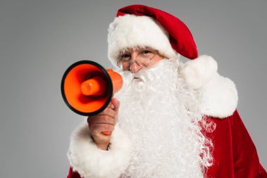 Gözlüklü Noel Baba hoparlörü tutuyor ve gri kameraya bakıyor. 