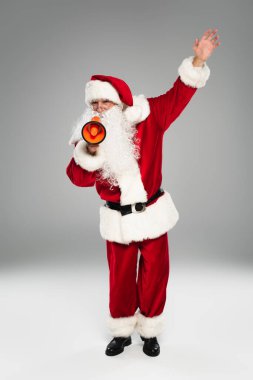 Kırmızı kostümlü Noel Baba 'nın tam uzunluğunda gri arkaplanda hoparlör var. 