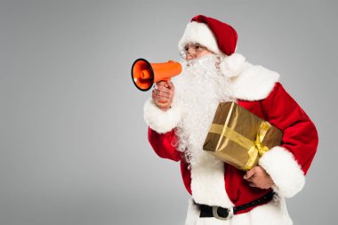 Gözlüklü Noel Baba hoparlörü tutuyor ve gri renkte izole bir şekilde duruyor. 